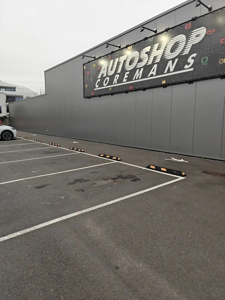 De parking naast de winkel, met de verlichte naam Autoshop Coremans op de gevel